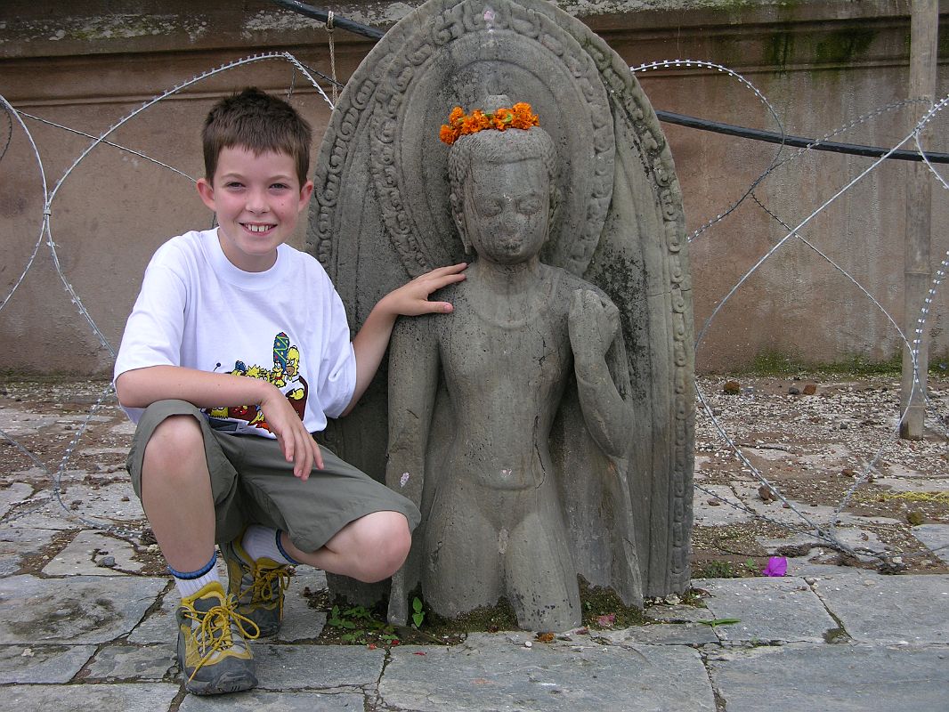 Kathmandu Pashupatinath 07 Peter Ryan With 7C Half-Buried Buddha Statue Peter Ryan poses with a 7th century statue of Buddha carved on a stele and half-buried amid the flagstones at the Pashupatinath Hindu temple complex in Kathmandu Notice the pervasive military presence in 2005 with the barbed wire behind the peaceful Buddha.